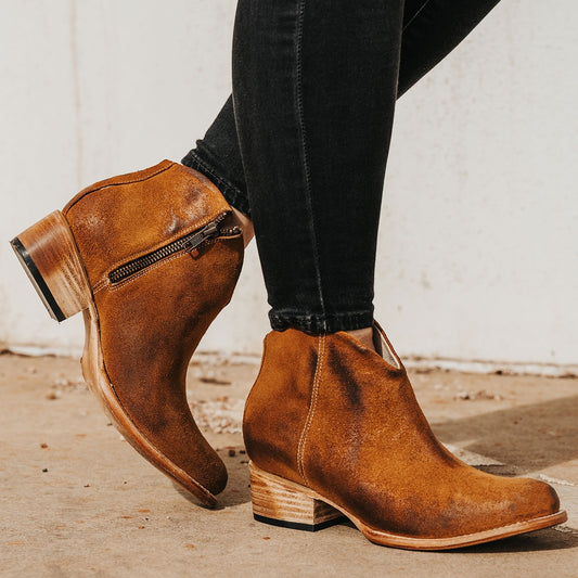 FREEBIRD women's Hippy cognac suede low heeled bootie with a working brass zip closure, heel seam embroidery, almond toe, and front dip detailing