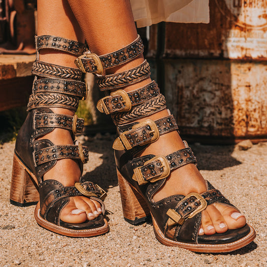 FREEBIRD women's Jett black leather sandal with adjustable gold buckling, a high lifted heel and metallic chevron stitching