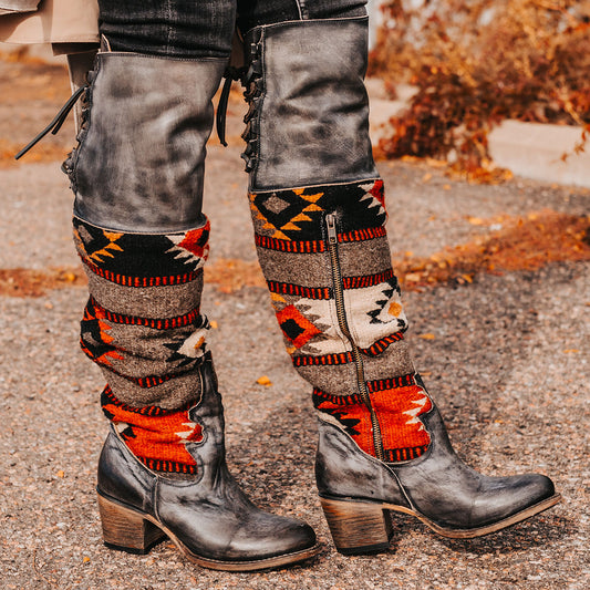 Stone SERAPE tall leather boots with intricate knit shaft, multiple buckle straps, and a distressed wooden heel.