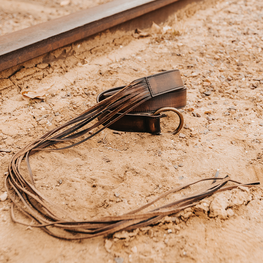 Black TASSEL BELT in distressed leather featuring an O-ring closure and long, functional fringed tassels.