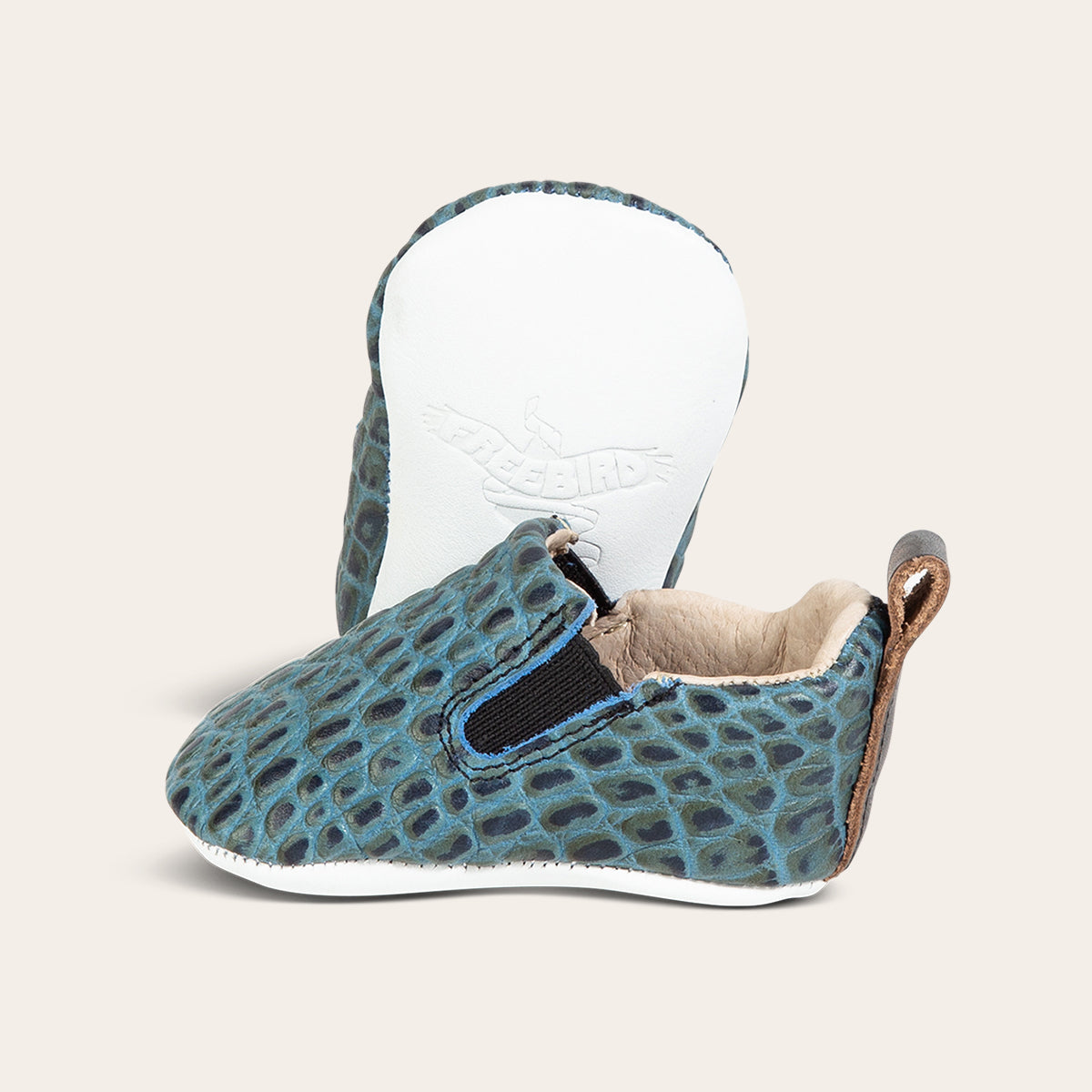 side view showing pull tab and side elastic panel and soft leather imprinted sole on FREEBIRD infant baby kicks turquoise croco leather shoe