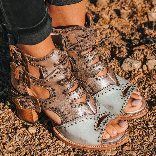 FREEBIRD women's Bradshaw blue/silver two-toned leather sandal with adjustable gold buckle hardware, stud embellishments and cut out detailing. Finished on a lifted high heel. 