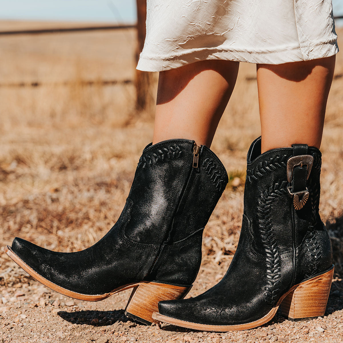 Black FREYA brushed suede boots featuring leather whip stitching, a snip toe, and an embossed metal buckle.