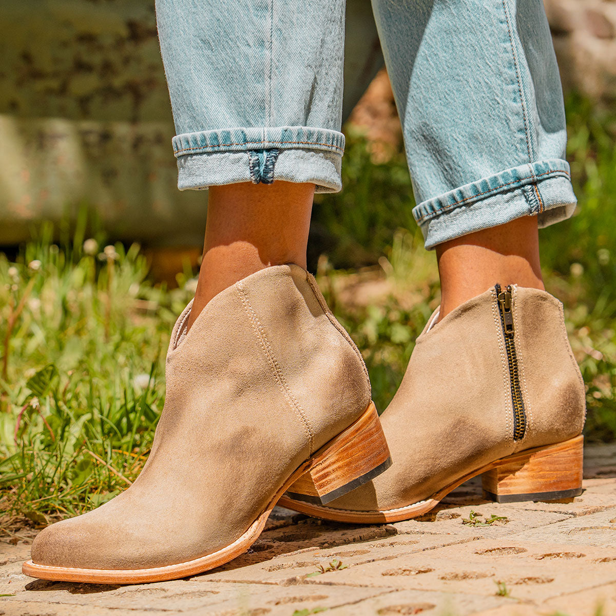 FREEBIRD women's Hippy beige suede low heeled bootie with a working brass zip closure, heel seam embroidery, almond toe, and front dip detailing