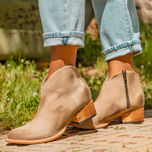 FREEBIRD women's Hippy beige suede low heeled bootie with a working brass zip closure, heel seam embroidery, almond toe, and front dip detailing