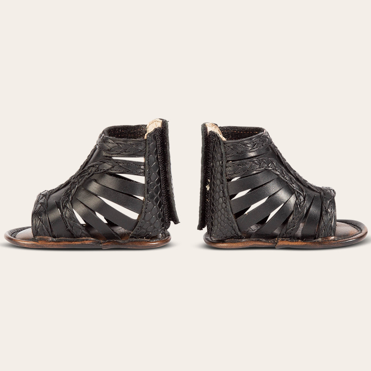 side view showing laser-cut leather, braided accents and embossed leather back velcro panel on FREEBIRD infant baby bela black leather sandal