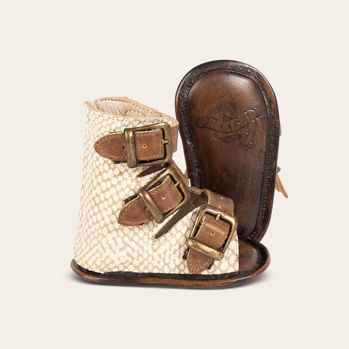 side view showing buckle fashion straps and soft leather imprinted sole on FREEBIRD infant baby bond white snake sandal