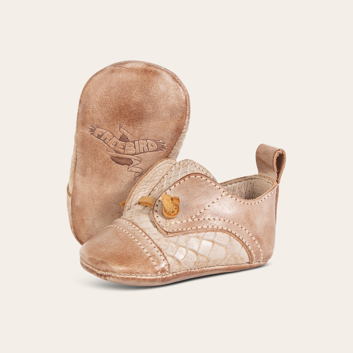 side view showing decorative knotted leather lace and soft leather imprinted sole on FREEBIRD infant baby mabel taupe leather shoe