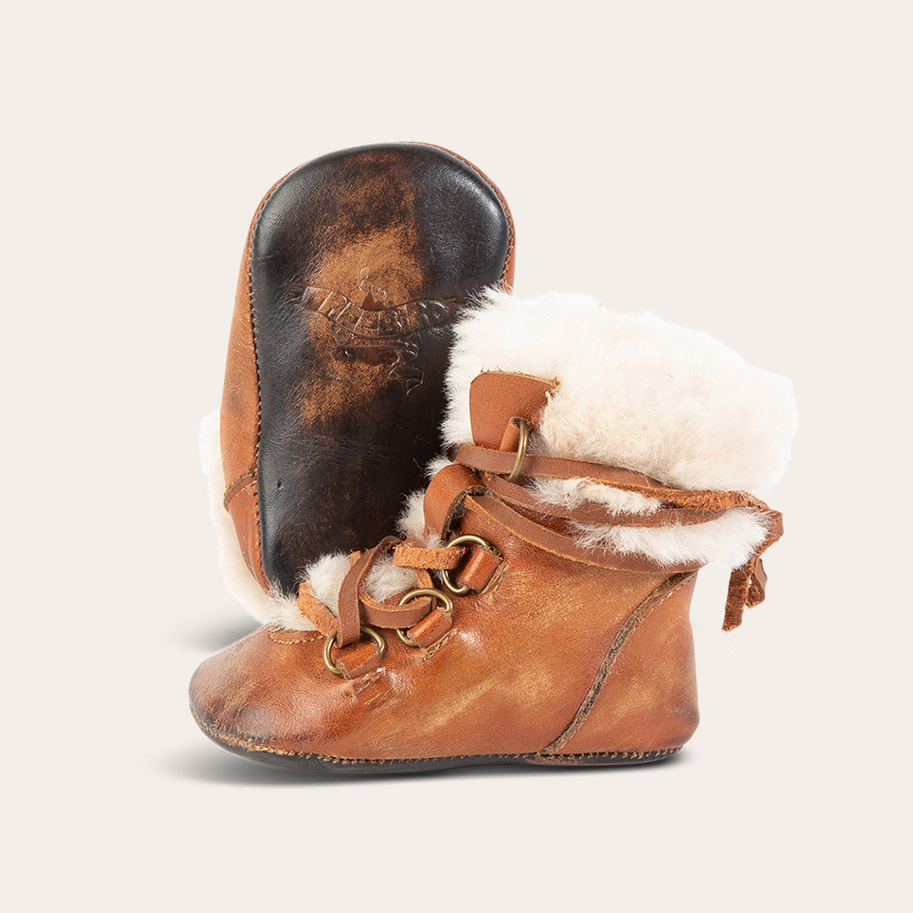 Side view showing shearling lining and contrasting leather lace detailing and soft leather imprinted sole on FREEBIRD infant baby Norway cognac leather bootie
